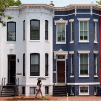 A woman with an umbrella walks past red, white and blue painted row houses.