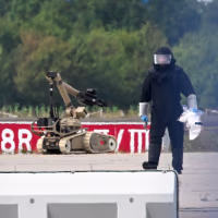A forensic technician works alongside a bomb-disposal robot.