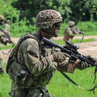 Luke Lem in his army uniform carries a gun while walking in a field