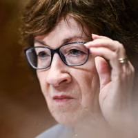 Susan Collins adjusts her glasses while seated