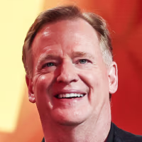 Roger Goodell smiles on stage while holding a folded suit in his hands