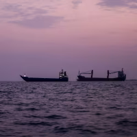 Three commercial vessels floating in the water at sunset.