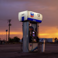 A lone gas pump is illuminated as the sun sets in the background.