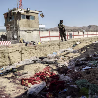 A lone Taliban soldier stands over a pile of scattered clothing. 
