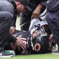 Caleb Williams lying on his back on the field, surrounded by Bears staff.