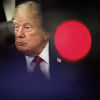 President Trump is partially obscured by a blurred foreground with a bright red dot.