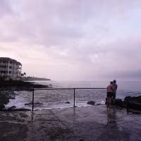 A couple observing a purple sunset over a cloudy sky on the Hawaiian coastline.