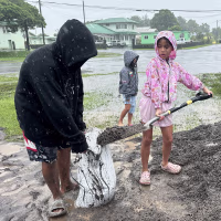 A young girl shovels wet sand into a sandbag in the rain.
