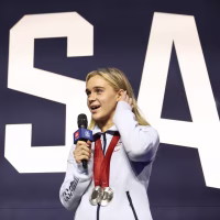 Alexandra Truwit speaking on a stage with two Olympic medals around her neck.