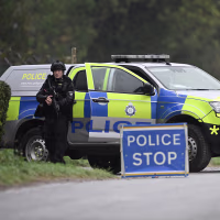 Two police officers in black tactical gear standing near a law enforcement vehicle.