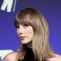 Taylor Swift poses against a blue step-and-repeat backdrop.