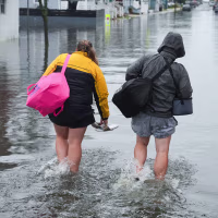 Mark F. And Carissa L. walk on a flooded street carrying bags and other belongings