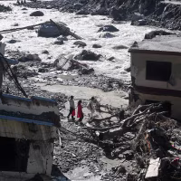 People walk past damaged houses.
