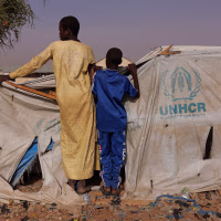 wo boys peer over a UNHCR aid tent at a camp in Chad for refugees from Darfur in Sudan