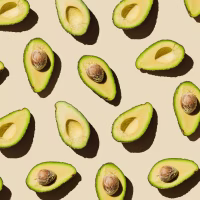 Pattern of fresh ripe green avocado fruit halves on beige background. Healthy food, diet and detox concept. Flat lay, top view