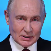 Vladimir Putin seen in a close view against an illuminated blue background.