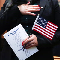 A person with their hand placed on their heart and the other hand holding an American flag and document with the star-spangled banner and pledge of allegiance
