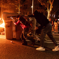 Trash containers burn in a central street at night near protestors