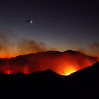 A firefighting helicopter flies over the Bryson Fire on October 15, 2026 in Malibu, California.