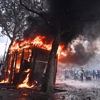 Image: A protester in Paris looks at a burning stand.