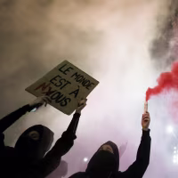 Protestors holding signs and waving smoke grenades at night.