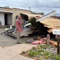 A man stands outside of a damaged house
