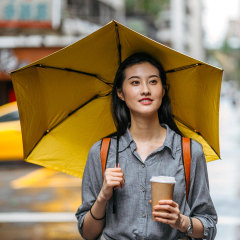 Woman walking outside with a cup of coffee, holding a yellow umbrella