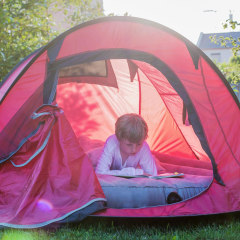 Boy reading in a red tent at evening twilight on an air mattress