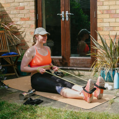 Woman sitting on a yoga may, exercising in her garden, using a resistance band