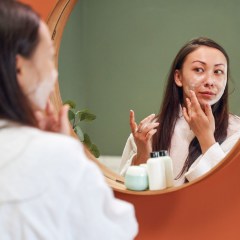 Woman applying moisture cream on her face, while looking in mirror