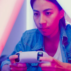 Young Asian woman playing video game console in neon lights living room at home. Gamer lifestyle concept.