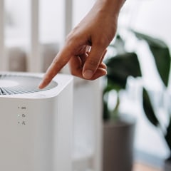 Close up hand of a mother turning on home air purifier for her newborn baby who is sleeping in the crib in the nursery. Fresh air. Cleaning and removing dust and bacteria. Healthier life and living concept