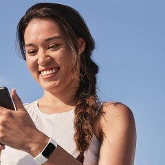 Woman with a Galaxy 5 watch, looking at her phone, Apple Watch and a white fitbit