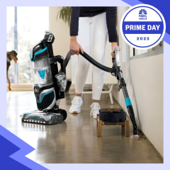 Hand using the Bissell SurfaceSense Pet Upright Vacuum to clean up pet food not he floor