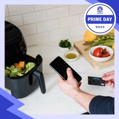 Man in kitchen shopping on his phone, while using an air fryer