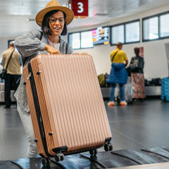 Beautiful young female tourist picking up her luggage from conveyor belt at the airport.