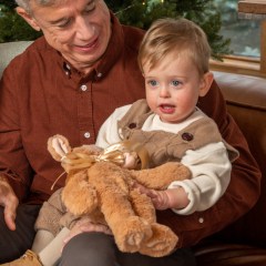 1 year old holding a stocking stuffer while sitting on his dad's lap.