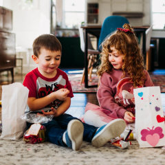 Two children sitting on the floor opening Valentines Day cards and gifts.