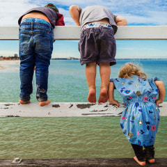 Rear view of siblings looking at sea while standing on railing against sky