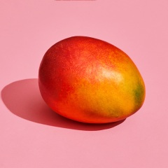 fresh whole mango on coral pink background, top view