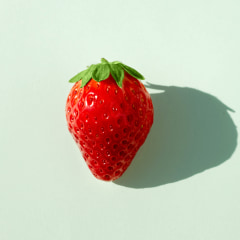 Strawberry in the middle of a soft green background with natural light and long shadows.