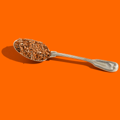 Spoon with flax seeds on the orange background