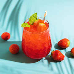 Summer refreshing sparkling drink with melted ice, fresh strawberry and drinking straw and mint in transparent glasses on blue background.