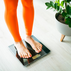 Close up of woman in orange sport clothes measure weight on scale.