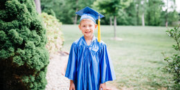 Portrait of happy boy in graduation gown standing at park