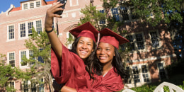 Happy college graduates taking photo with smartphone