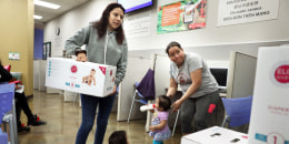 Monse Delgado (left) picks up diapers for her one year old Joe Yohander (middle) as Lupita Mendoza (right) waits for diapers for her one year old Jimena Sarci Rivas (with bottle) at the child care resource desk of the SF Human Services  Agency on Friday, Nov. 22, 2019, in San Francisco, Calif.  San Francisco this month became the first county in the US to hand out free diapers with its SNAP (food stamp) benefits.
