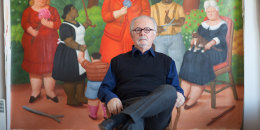 Fernando Botero sitting at his studio in front of a painting.