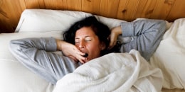 Woman with eyes closed yawning in bed at home