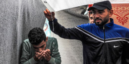 Men use their hands to drink rainwater dripping from the roof of a tent at a U.N.-run school in Gaza.